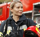 Portrait of young woman firefighter standing near fire truck.