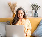 Beautiful mature woman sitting on yellow sofa while using her laptop at home. Woman concentrating while looking at new decorations for her home online.